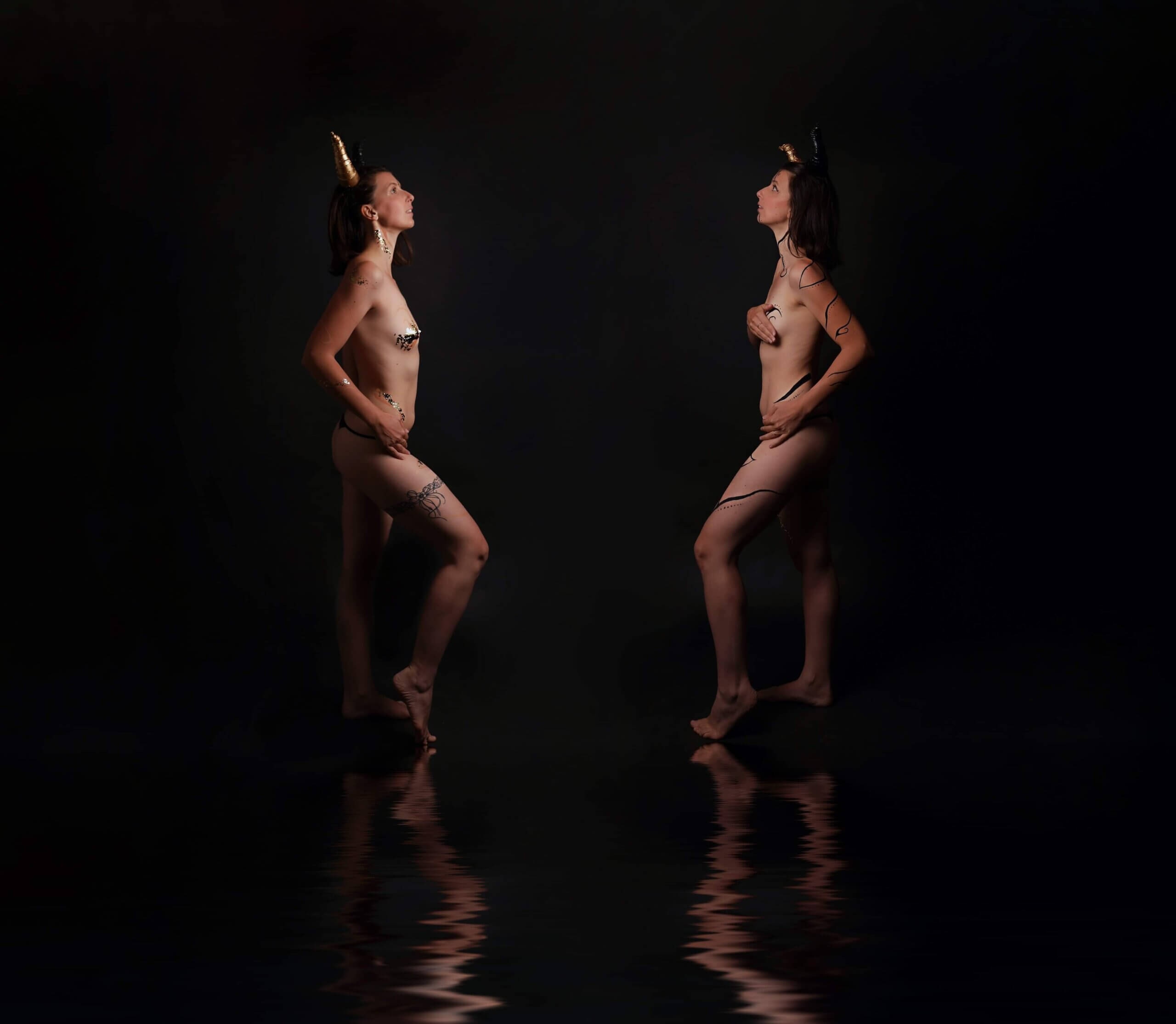 Une photographie artistique dramatique de deux femmes debout, dos à dos, dans un environnement sombre, avec des cornes dorées et des dessins corporels, reflétant la confiance et le mystère.