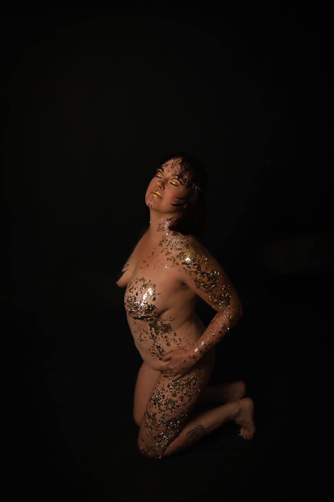 Une photographie artistique frappante d'une personne à genoux sur un fond sombre, ornée de paillettes dorées et argentées, capturant une pose dramatique qui dégage sérénité et confiance.