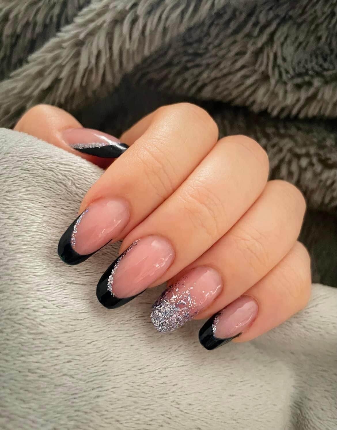Gros plan d'une main reposant sur une surface douce et texturée, mettant en valeur un nail art élégant avec une base nude naturelle et des pointes noires, ainsi qu'un effet dégradé de paillettes allant de l'argent au transparent.