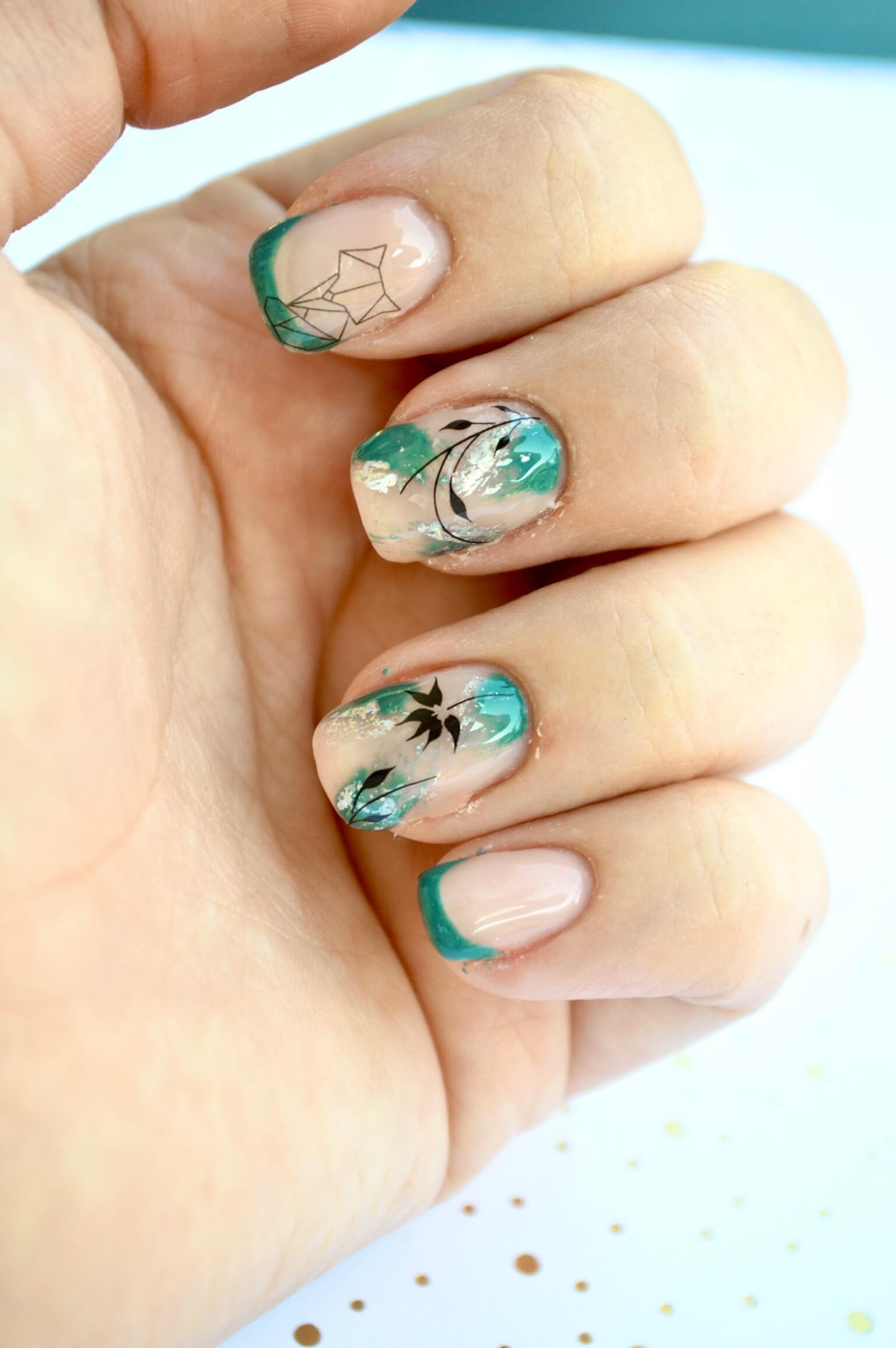 Gros plan d'une main affichant des ongles élégamment manucurés, avec une base beige clair ornée de designs teal complexes, y compris des formes abstraites et des motifs floraux en noir, les pointes étant peintes d'une couleur teal vibrante, sur un fond doux avec des points dorés éparpillés.