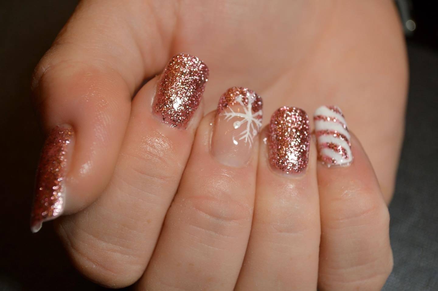 Gros plan sur une main avec des ongles magnifiquement manucurés, ornés de paillettes roses et dorées, d'un flocon de neige blanc et de rayures de canne en bonbon rouge et blanc, parfaits pour les célébrations des fêtes.