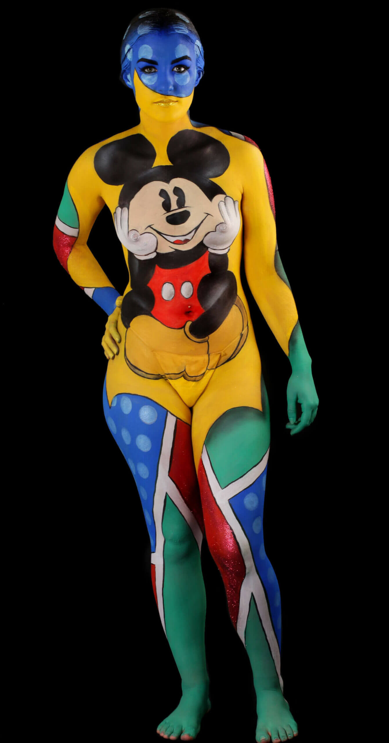 Un design peint vibrant sur tout le corps d'une personne, présentant des couleurs bleu et jaune d'un côté, avec des pois colorés en rouge, vert et bleu. Le torse est orné d'une grande illustration de Mickey Mouse sur un fond noir, mettant en valeur l'aspect ludique et artistique de la peinture corporelle.