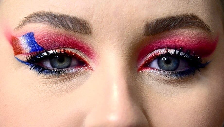 Gros plan sur des yeux époustouflants ornés d'un maquillage artistique audacieux avec des nuances vibrantes de rouge et de rose, des accents métalliques argentés et bleus, des lignes de paupières nettes, et un mascara noir dramatique, mettant en avant un design de maquillage de festival unique et expressif.